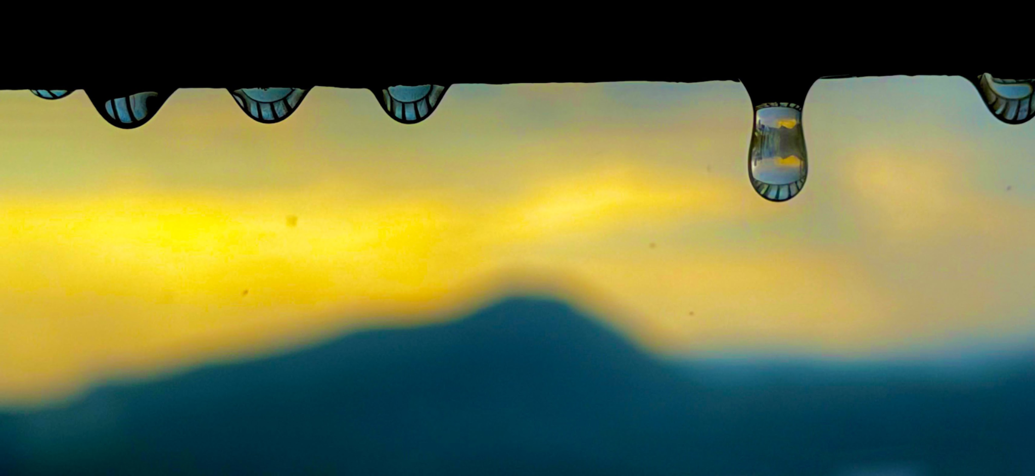A close landscape photograph of water droplets reflecting a golden-blue scene